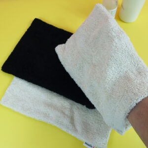Bamboo spa mitt worn by a hand, hovering over a black mitt on top of another unbleached mitt.
